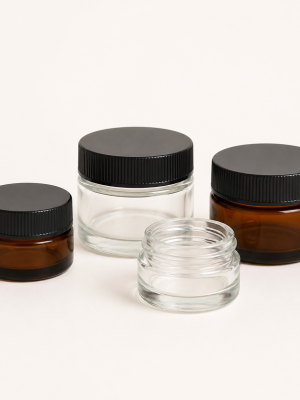 Clear and amber glass ointment jars with black ribbed screw lids